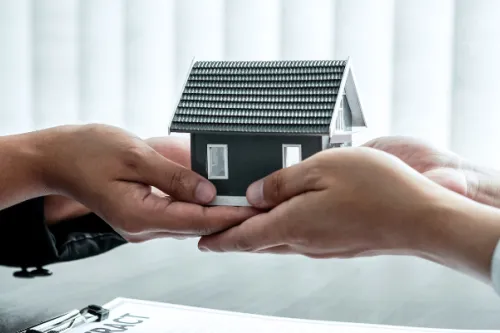 Duas pessoas a trocar uma casa miniatura com o logotipo Maxfinance 